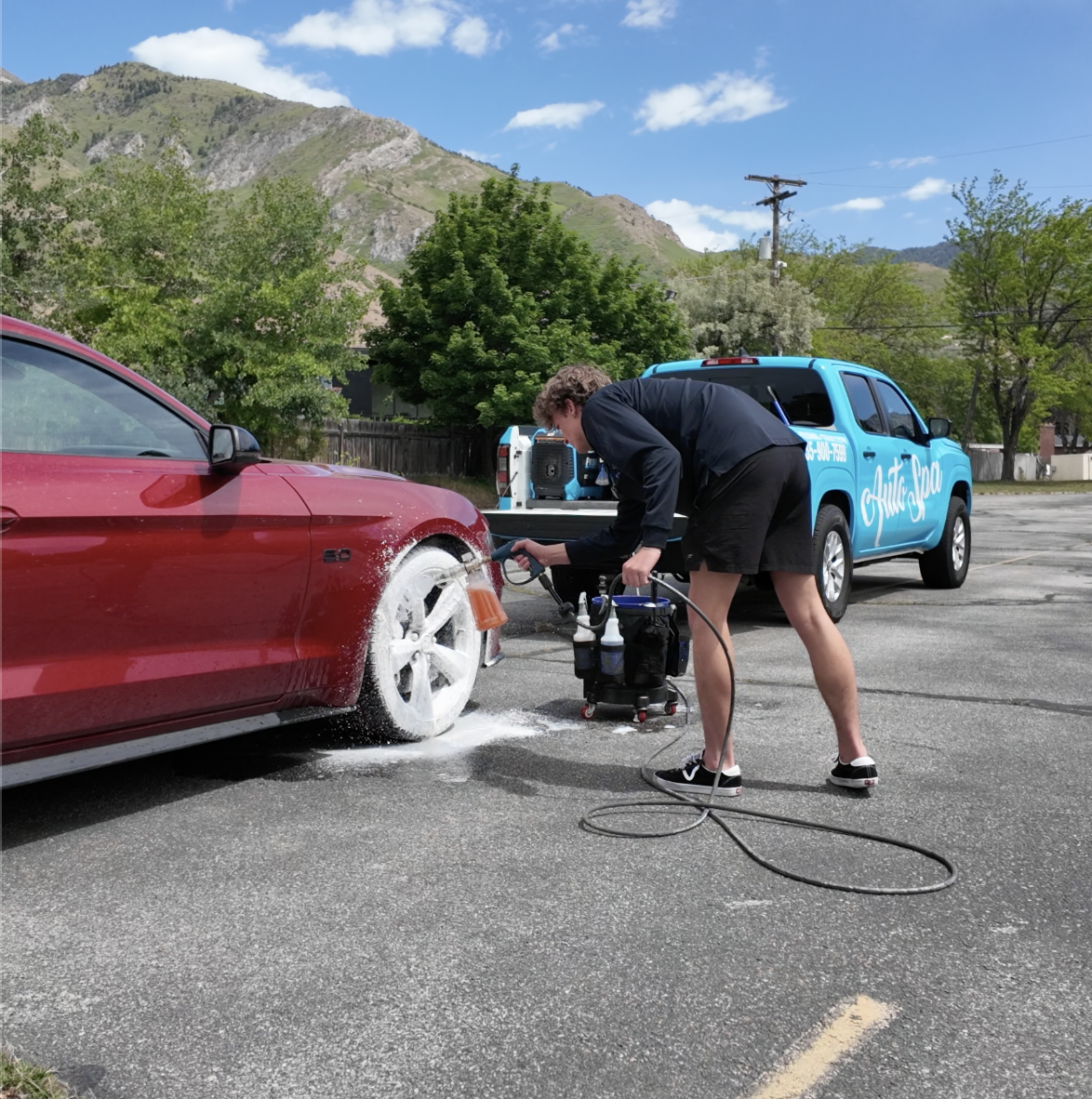 The Auto Spa technician detailing a red Ford Mustang wheel in Salt Lake City with branded mobile unit and Wasatch Mountains
